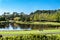 Garden seat overlooking large duck pond in community parkland filled with green trees and walkways including bridge over water aga