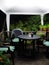 Garden seating area covered by a white gazebo at night lit by bright white light with pot plants and decking