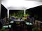 Garden seating area covered by a white gazebo at night lit by bright white light with pot plants and decking