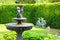 Garden with small fountain and stone bench green lawn plants trees