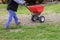 Garden worker with sowing lawn grass seeds with a drop lawn spreader in the residential backyard