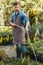 Gardener in apron and rubber boots watering plants with sprinkler in garden