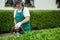 Gardener clipping hedge in garden using petrol hedge cutter.