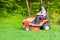 Gardener driving a riding lawn mower in garden