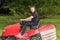 Gardener driving riding lawn mower in garden