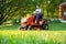 Gardener driving a riding lawn mower in garden