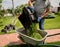 Gardener emptying lawn mower grass into a wheelbarrow after mowing.