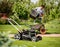 Gardener emptying lawn mower grass into a wheelbarrow after mowing.