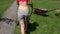 Gardener female woman in bra and shorts push mower near stone path. 4K