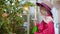 Gardener girl in pink hat spraying plants in indoor orangery. Young female florist spraying ficus tree in flower salon.