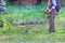 A gardener mows a green lawn with a petrol trimmer on a summer day