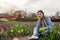 Gardener relaxing among fresh tulips, daffodils, hyacinths in spring garden. Happy woman admires colorful flowers