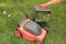 A gardener`s hand holds a lawn mower box next to lawn mower on grass