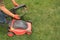 A gardener`s hand holds a lawn mower box next to lawn mower on grass