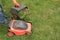 A gardener`s hand holds a lawn mower box next to lawn mower on grass