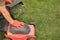 A gardener`s hand holds a lawn mower box next to lawn mower on grass