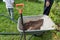 A gardener standing near wheelbarrow and a shovel on the lawn of a garden, gardening and horticulture concept