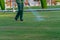 A gardener is watering the lawn at a tropical resort. Man watering green lawn, sprinkling water on the grass with water