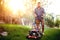 gardener working with lawnmower and cutting grass in backyard during summer sunset