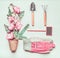 Gardening composing with sign, tools, pink gloves, pink flowers and plant pots, shovel at light green background, top view