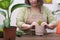 gardening woman in apron caring potted houseplant in a greenhouse surrounded by plants