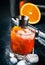 Garibaldi alcoholic cocktail with red bitter, orange juice, zest and ice. Dark blue background, bar tools, selective focus