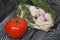 Garlic in an overturned wicker basket. Dill sprigs and tomato. On black pine boards. Close-up shot