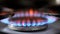 Gas burner with bright red and blue flames on kitchen stove on dark blurred background.