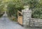 Gate post with wooden gate open to a long driveway