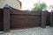 Gates and wicket of brown color on the brick fence in front of the house