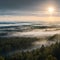 The Gauja river valley and pine forest are shrouded in a thick fog at sunrise.