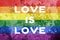 Gay rainbow flag with horizontal stripes on concrete background with love is love text