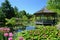 Gazebo in Lush Green Field, Serene Haven for Relaxation and Gathering, A flower-filled gazebo overlooking a calm pond filled with