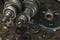 Gear wheels, damaged modes lie on a wooden table top. In the background a manual transmission from the car.