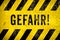 GEFAHR! in German, danger warning sign text with yellow and black stripes painted over concrete wall cement texture background