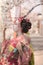 Geisha in kimono posing in profile admiring cherry blossoms at su