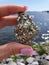 Gems Stone Cluster Crystal Pirite Pyrite. Fools Gold in hand of woman with pink nails. Backgroundlake ocean water sky