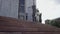 A general slow motion shot of a young dark-haired woman exiting the buidling and walking down the stairs, passing the