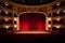 General view of an empty opera or performing arts theater. Rows of red seats and red curtain with lighted lamps