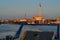 General view from ferry of an industrial harbor with moored large ships with masts, barges with cargo, boats in red light of sunse