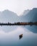 Generative AI Illustration of beautiful mountain range and lake with boat in lake, soft misty sky at sunrise