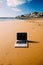 Generic notebook laptop on sunny deserted sandy beach background