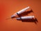 Generic, standard design single use plastic syringes with shadows due to back lighting. Orange color background.