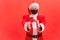 Generous elderly santa claus in eyeglasses and protective mask on face holding and showing gift box with red bow, making present