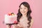 Generous woman holding birthday cake front pink background