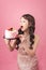 Generous woman holding birthday cake front pink background