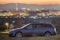 Geneva, Switzerland - October 9, 2018: Gray car moving at night in green meadows on background of lights of distant city buildings