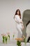 gentle brunette in white stands in a room with bouquets of tulips on the floor