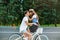 Gentle couple in love on bike on road on forest background. Handsome guy in white T-shirt is driving a bike, girl with