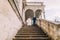 Gentle groom holding hands when going down with his pretty bride by antique palace stone stairs. Low angle shot